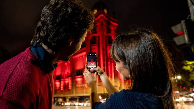 Paint the Town Rouge promo image of a couple photographing a building