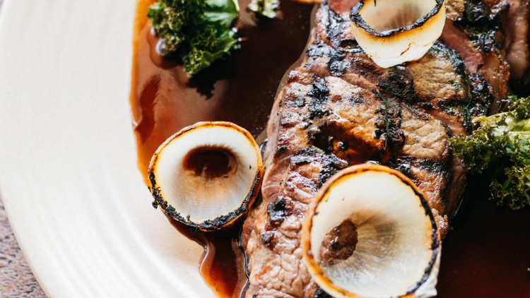 A grilled sliced steak with charred onion rings, kale and sauce