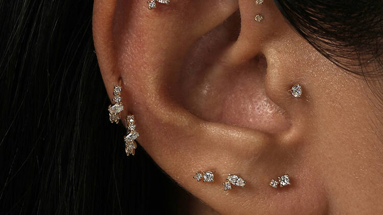 A close-up of a woman's ear featuring several diamond and gold piercings.