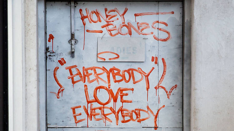A blue door with red graffiti that reads 'Honey Bones - everybody love everybody.' 