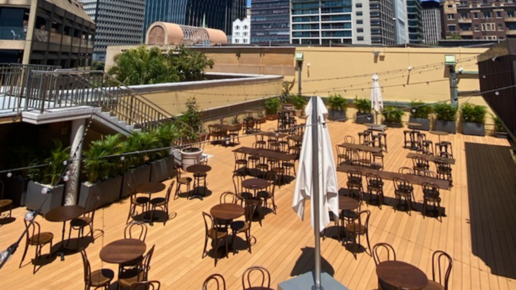 A rooftop bar with light wooden timber flooring, round table and bent cane chairs