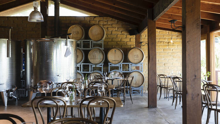 A dining area with tables and seats, and wine making apparatus visible in the backdrop.
