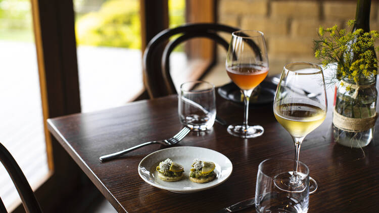 A table setting at Avani Wines that includes a dish with two canapes and a glass of wine.