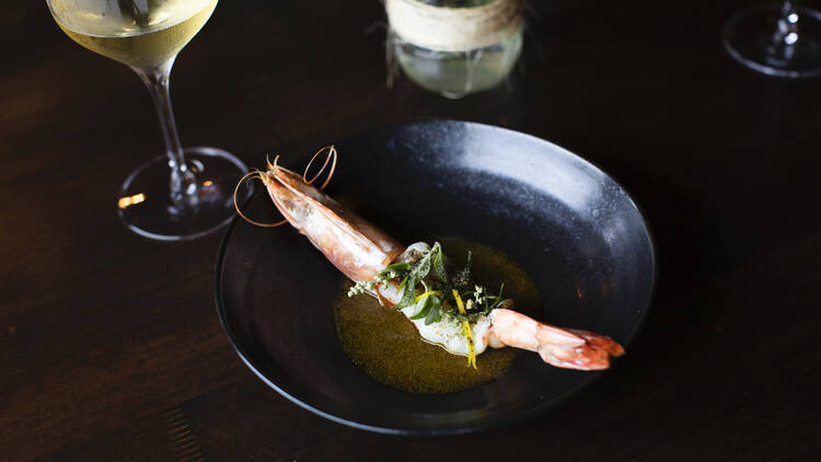 A close-up of a dish consisting of shrimp topped with fresh herbs in a buttery sauce.