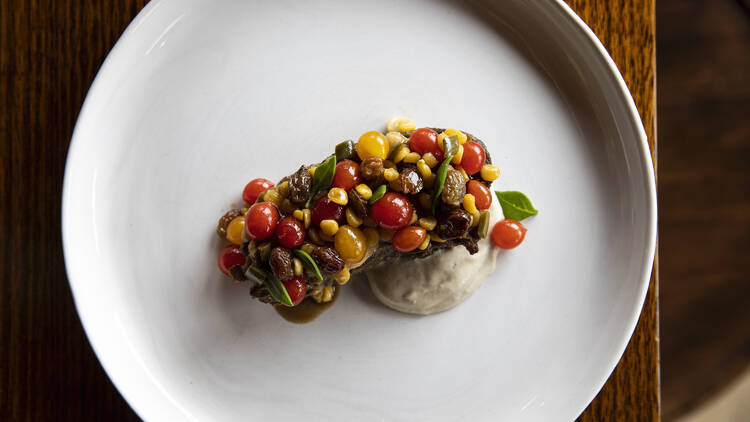 A close-up of a white plate topped with a dish consisting of fresh vegetables and nuts and a cream base.