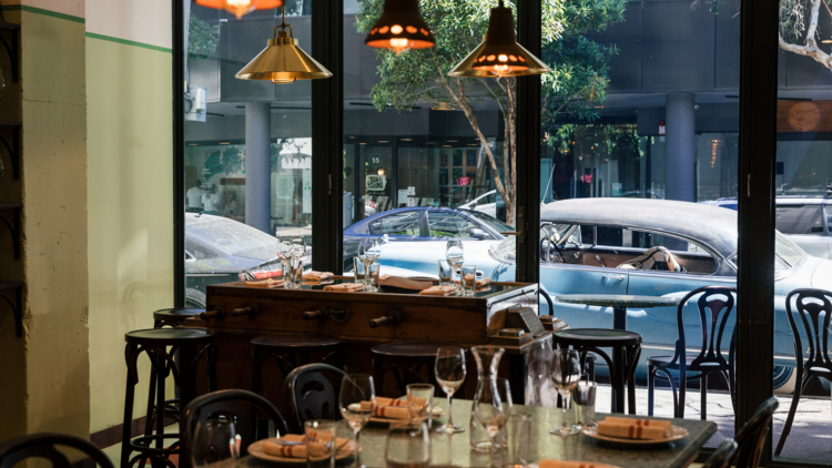 An empty restaurant with hanging pendant lights, green tables, bentwood chairs