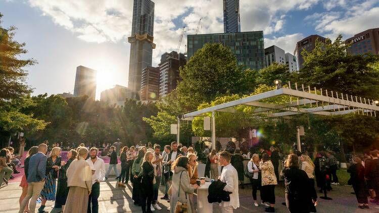 A crowd of people enjoying the NGV sculpture garden on a sunny evening