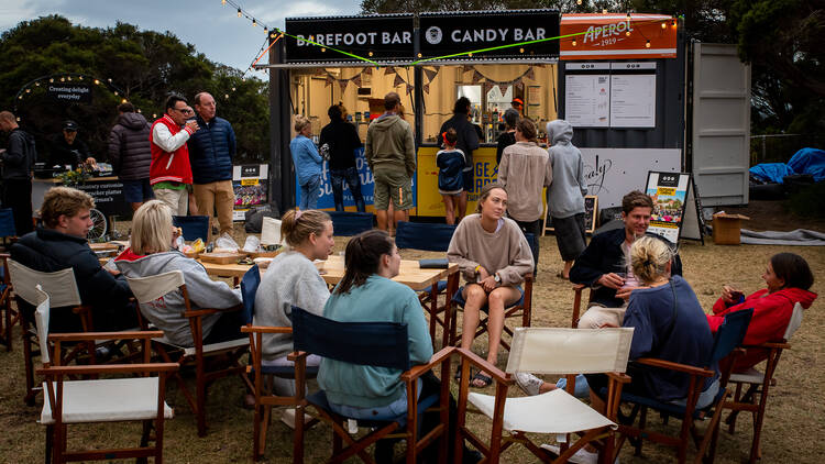 A group of people sitting at outdoor tables with a bar in the background.