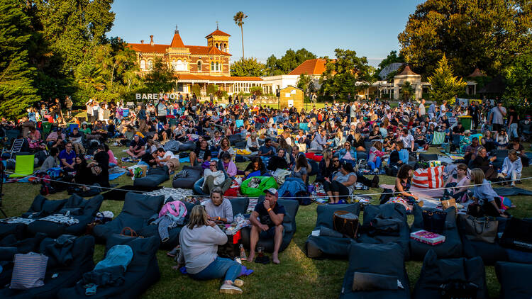 A faraway shot of a crowd of people sitting on beanbag chairs on a park lawn at Barefoot Cinema.