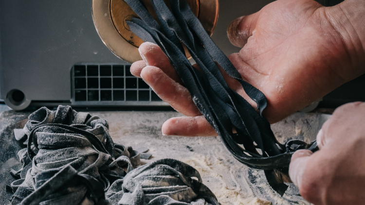 Black pasta being churned out by a machine