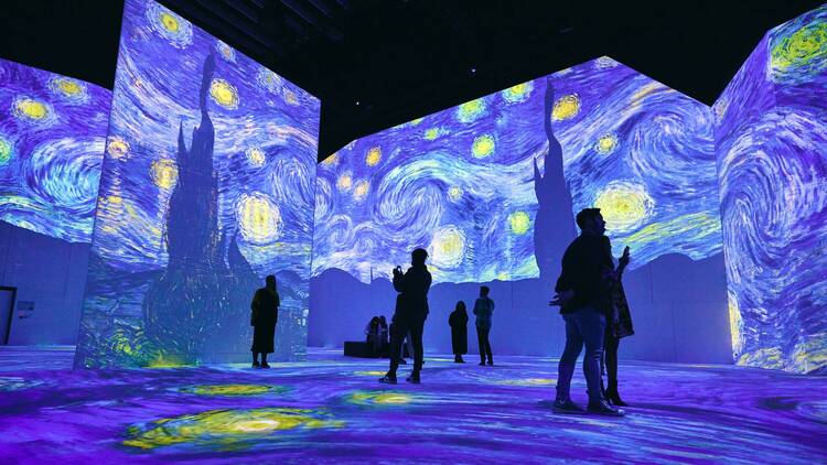 A vast gallery space with Vincent Van Gogh's The Starry Night painting projected on the walls.