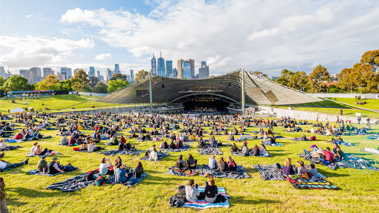 A wide shot of the Sidney Myer Music Bowl on a sunny day with groups of people sitting on the lawn