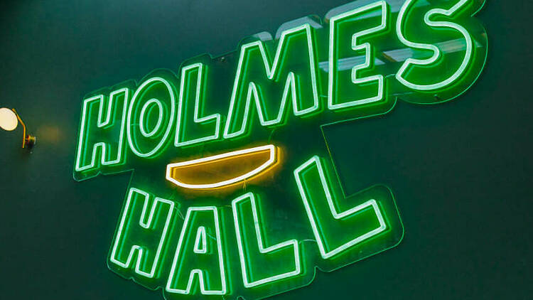 A green neon sign that says Holmes Hall.