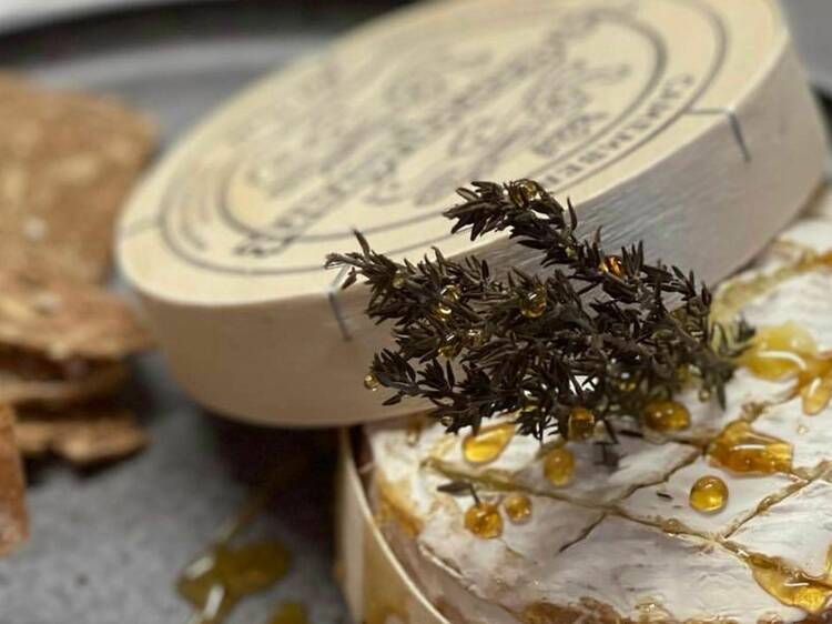 A close-up shot of a soft cheese covered with honey and topped with rosemary.