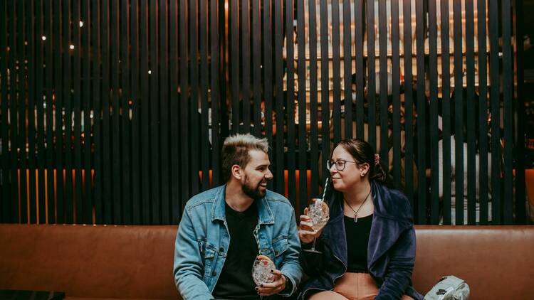 A man and a woman sitting at a leather booth inside the Distiller.