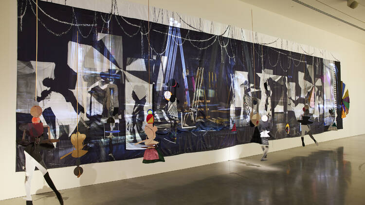 An installation by Sally Smart featuring a large, long abstract image hung on a wall with various abstract cutouts dangling in front of it