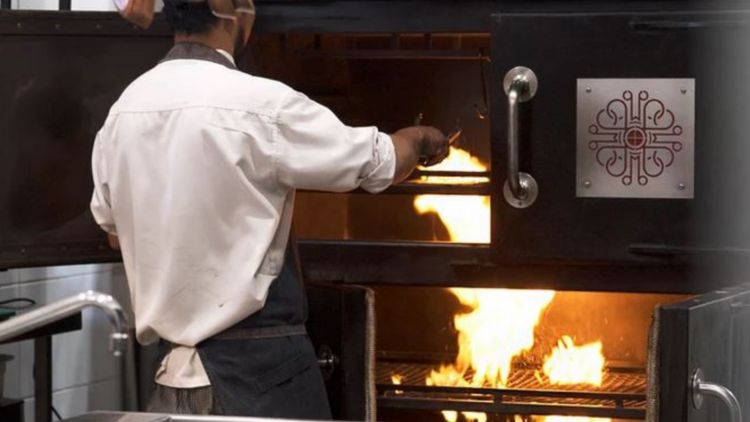 A chef is tending to food within a large black smoker