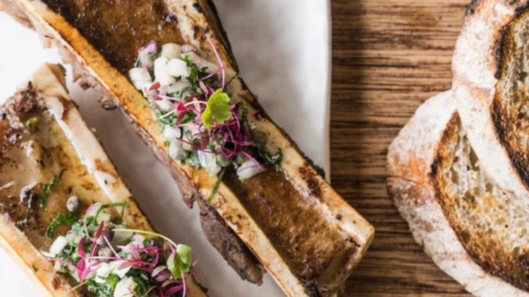 Grilled bone marrow with inions and microherbs next to grilled bread