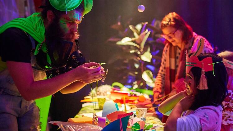 Kids wearing colourful paper masks interact with an adult in a fun green sparkly outfit at a dance party