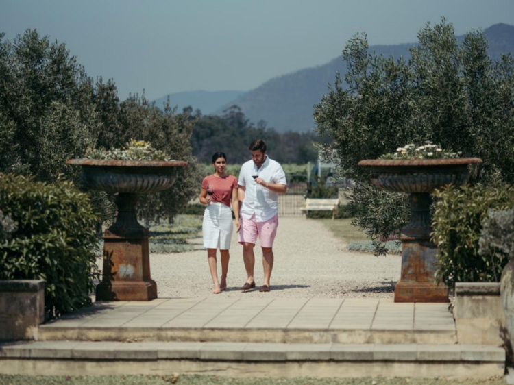 A couple walking through the gardens of Margan with a glass of wine