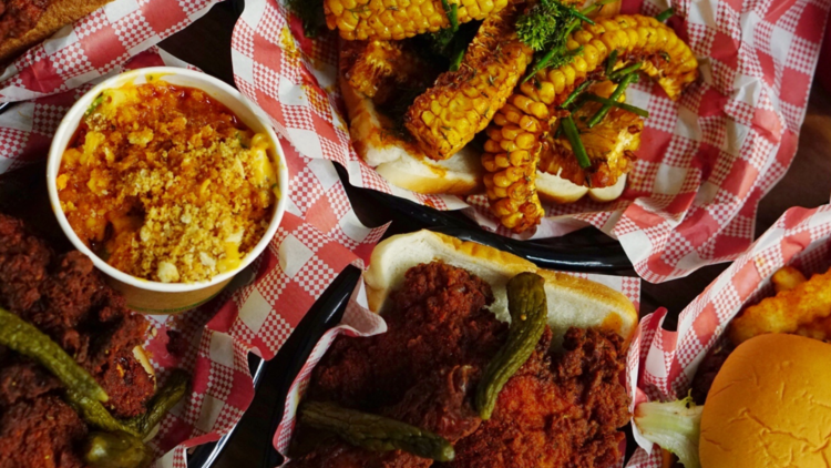 A flat lay of fried chicken, mac and cheese, corn ribs and burgers on gingham paper