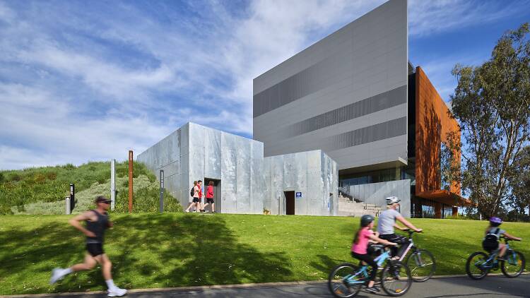 The outside of SHepparton Art Museum on a sunny day with walkers and cyclists going past 