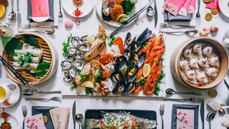 A flat lay of a chinese banquet with steamed fish, dumplings, seafood and spring rolls