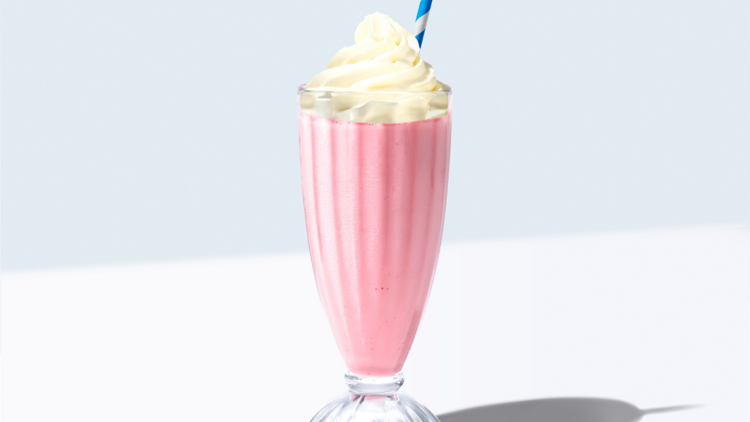 A strawberry milkshake with whipped cream, a blue and white straw