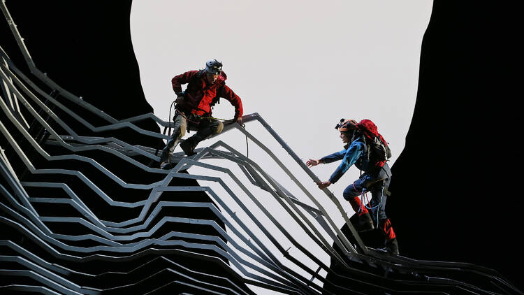 Two people climb on a steel girder mountain as part of Touching the Void