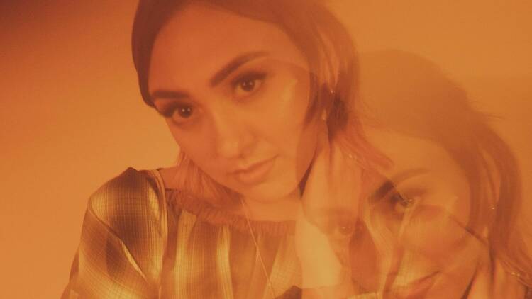 Alice Skye posing coyly. An orange filter has been laid over the photograph, with a double exposure of Skye visible in the corner of the image