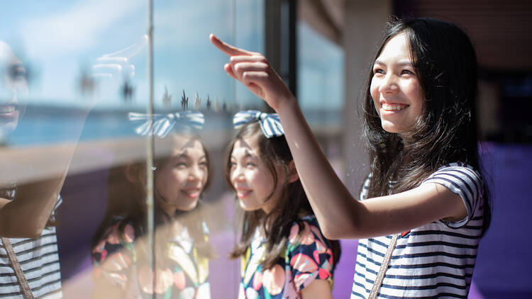 Two children look through a window and point to something in the distance.