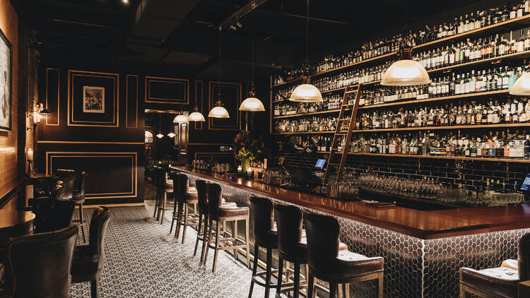 A dimly-lit whiskey bar with intricate wood panelling and an entire shelf of alcohol.