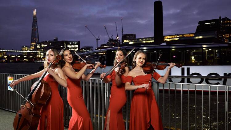 people wearing red dresses playing the violin by the Thames