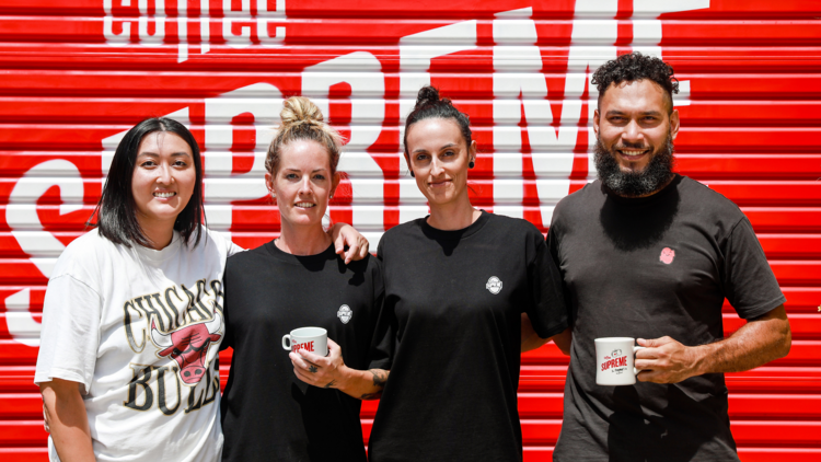 Four team members of Coffee Supreme stand in front of a red painted rollerdoor