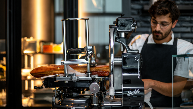 A chef slicing meat on a deli slicer