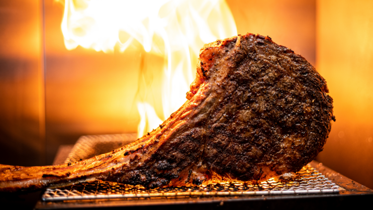 A huge steak on the grill with flames