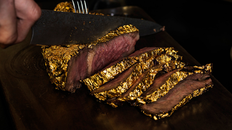 A huge steak being sliced with gold leaf