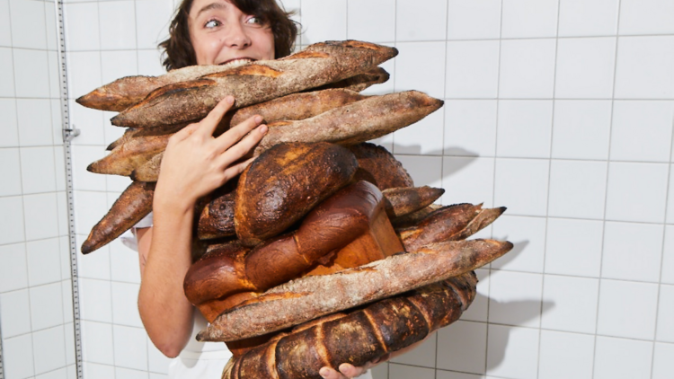 A baker struggles to hold a stack of loaves