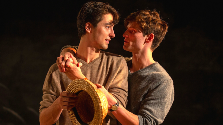 Breaking the Code at New Theatre. Two young men share an embrace, one holds a straw hat.