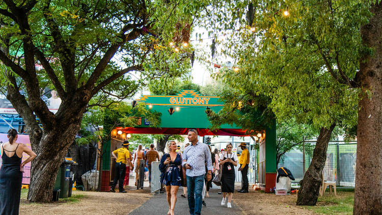 A man and a woman walk through a festival entrance that says 'Gluttony' on the sign.