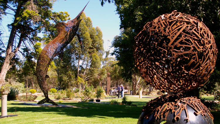 A giant sculpture of a swordfish and an orb made out of rusty spanners in a sunny park