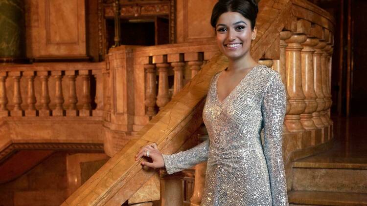 Actress Shubshri Kandiah poses next to a grand staircase in the Capitol Theatre while wearing a sparkly gown