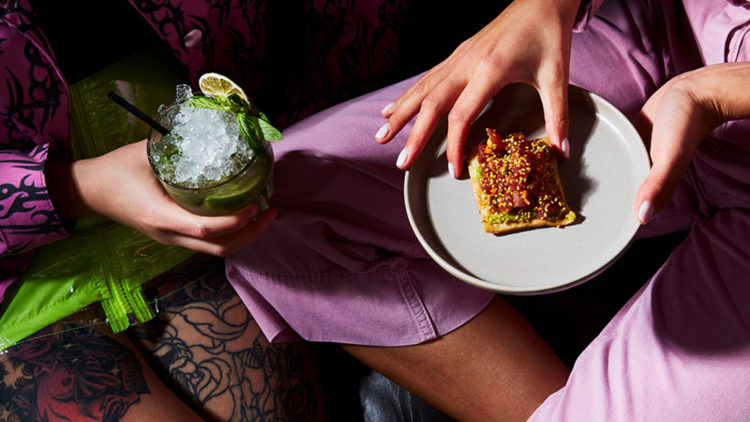 Two people wearing pink are eating a snack and drinking a cocktail