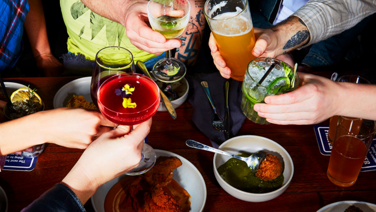 People cheersing their drinks over a table with plates of Indian snacks