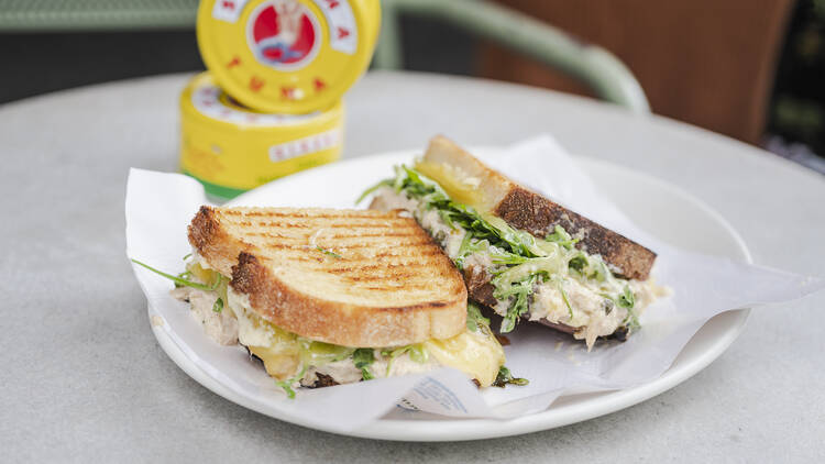 A tuna melt sandwich by King and Godfree on a plate, with tuna cans behind.