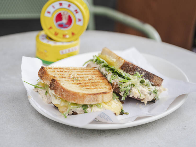 A tuna melt sandwich by King and Godfree on a plate, with tuna cans behind.