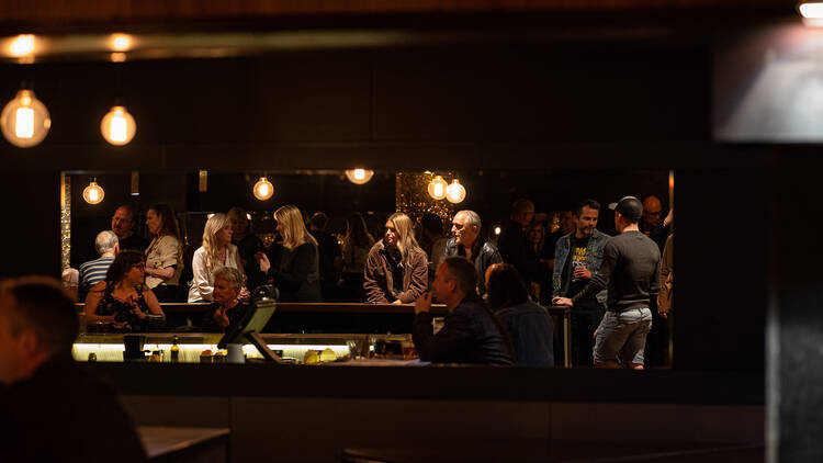 People standing around a dimly-lit bar.