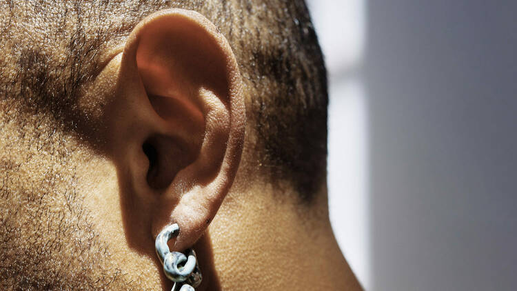 A close up of an ear on a head with shaved hair and a thick chain earring