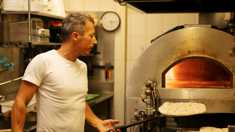 A pizziaola putting dough into an oven