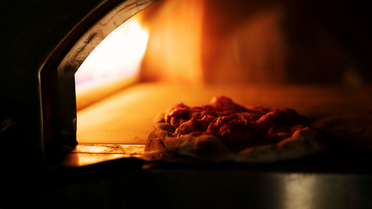 A pizziaola putting dough into an oven